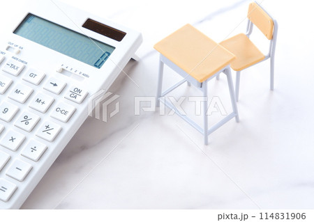 学校の机と椅子、電卓がイメージする、高騰を続けて家計を圧迫する教育費のイメージ 114831906
