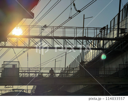 Silhouetted person walking on pedestrian bridge at sunset 114833557