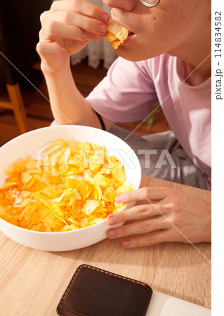 Caucasian person in pink t-shirt holding plate full of potato chips, young male eating potato chips 114834582