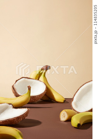 Vertical photo was taken from front with light yellow background, brown color table top containing plenty coconut and banana with empty space in the middle. Space for designing and adding text 114835205