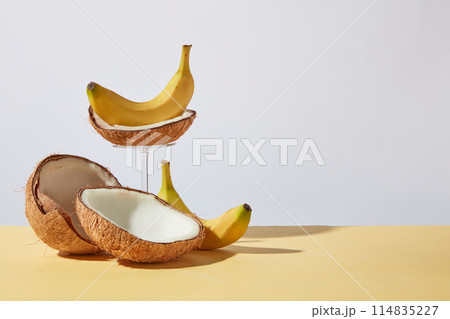 Promotion photo with coconut and banana ingredient featured on left side on yellow table over white background. Photo was shot from front with the blank right side for adding elements of design 114835227