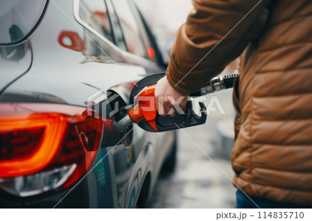 At a gas station, a person in a yellow jacket is fueling up a car using a fuel nozzle 114835710