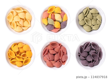 Conchiglie rigate, types of shell shaped and furrowed Italian pasta in white bowls. Uncooked durum wheat semolina pasta. Uncolored, mixed, colored with spinach, turmeric, beetroot, and black carrot. Conchiglie rigate, types of shell shaped and furrowed Italian pasta in white bowls. Uncooked durum wheat semolina pasta. Uncolored, mixed, colored with spinach, turmeric, beetroot, and black carrot. 114837918