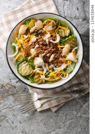 Cheeseburger salad with romaine lettuce, ground beef, pickles, cheddar cheese and croutons close-up in a bowl. Vertical top view 114838046