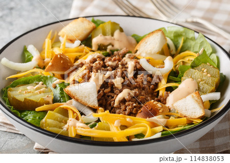 American Cheeseburger Salad with romaine lettuce, ground beef, pickles, cheddar cheese, onions and dressed with a special burger sauce closeup on the bowl. Horizontal 114838053