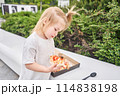 Cute happy girl cuts and eats in the park. Baked a delicious pizza Margarita in a traditional wood-burning oven in a Neapolitan restaurant, Italy. Pizza delivery concept in a cardboard box.  114838198