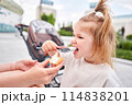 A hungry child enjoys eating ice cream outdoors. Portrait of a cute baby licking a creamy ice cream while walking in a city park, outdoor activities. 114838201