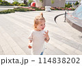 A hungry child enjoys eating ice cream outdoors. Portrait of a cute baby licking a creamy ice cream while walking in a city park, outdoor activities. 114838202