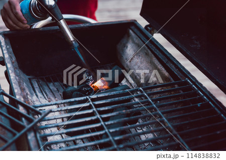 Man using BBQ lighter torch to start fire for charcoal. Man using BBQ lighter torch to start fire for charcoal. 114838832