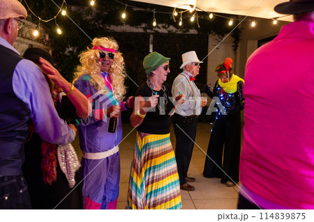 Adults in colorful costumes at a fun party, dancing under lights with music and laughter 114839875