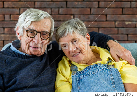 A senior couple embracing on a sofa in their cozy home, showing love and affection for each other A senior couple embracing on a sofa in their cozy home, showing love and affection for each other 114839876