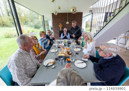 A family is gathered around the dining table in a modern home, enjoying a meal together 114839901