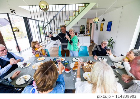 Senior friends enjoying food and drink in a modern dining room, sharing joy and happiness Senior friends enjoying food and drink in a modern dining room, sharing joy and happiness 114839902