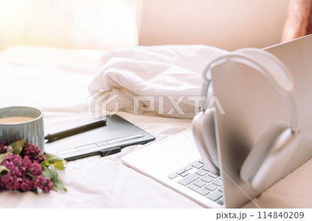Cozy workplace with wireless headphones hanging on laptop Cozy workplace with wireless headphones hanging on laptop 114840209
