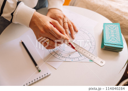 Woman drawing with pencil and ruler on natal chart 114840284