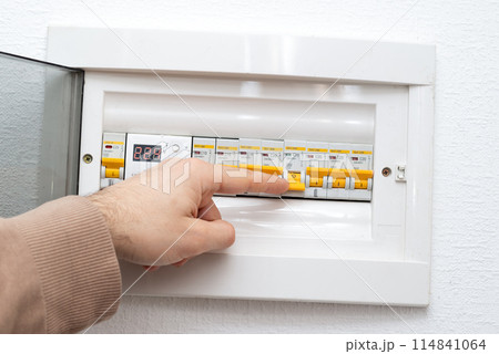 Hand is turning on circuit breaker on control panel after it tripped due to overload 114841064