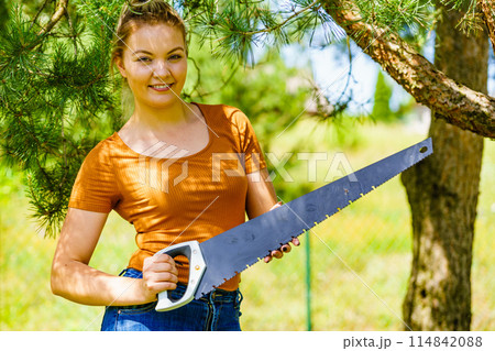 Female cuts branches of tree, using saw Female cuts branches of tree, using saw 114842088