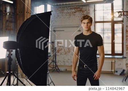 Young man in a black t-shirt posing in a photography studio. Professional photoshoot setting. 114842967