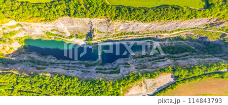 An aerial view of the abandoned limestone quarry Velka Amerika in Czechia, revealing clear, turquoise water surrounded by lush greenery and rugged rock formations. An aerial view of the abandoned limestone quarry Velka Amerika in Czechia, revealing clear, turquoise water surrounded by lush greenery and rugged rock formations. 114843793