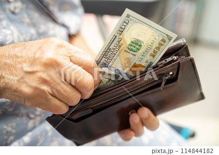 Asian senior woman holding and counting US dollar banknotes money in purse. Poverty, saving problem in retirement. 114844182