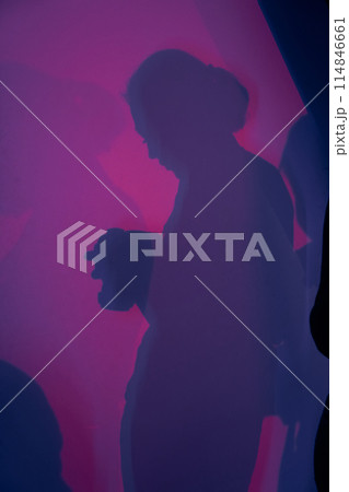 The shadow of a female photographer looking at a camera. Abstract gradient pink and purple background. The silhouette of a man, diffused light. High quality photo 114846661