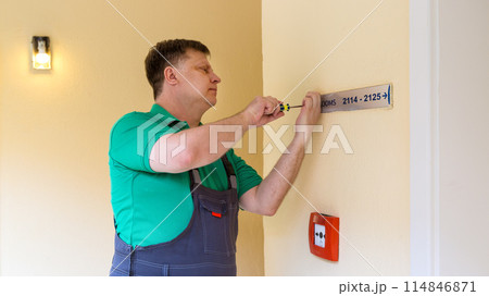 A male hotel worker screws a signpost to the wall A male hotel worker screws a signpost to the wall 114846871