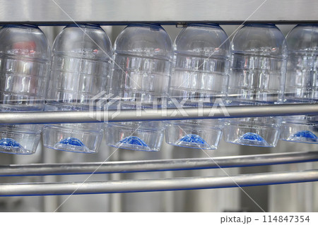 The  empty drinking water bottles  hanging on the conveyor belt for filling process. 114847354