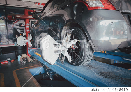 Car wheel balancer calibrate with laser reflector attach on each tire to center driving adjust. Car in auto service. Balancing tire wheel machine. Car wheel balancer calibrate with laser reflector attach on each tire to center driving adjust. Car in auto service. Balancing tire wheel machine. 114848419