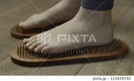 Female feet standing on boards with nails, close up. Media. Barefoot female standing on yoga nails board. Female feet standing on boards with nails, close up. Media. Barefoot female standing on yoga nails board. 114848540