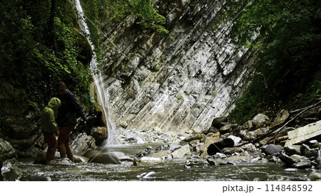 Beautiful waterfall in green forest. Creative. Mother and boy crossing tropical river in mountain jungle. 114848592