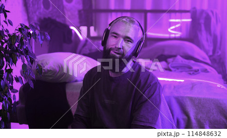Music lover, young man in headphones, neon light portrait. Media. Relaxed guy in wireless headphones putting them off. Music lover, young man in headphones, neon light portrait. Media. Relaxed guy in wireless headphones putting them off. 114848632