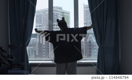 Relaxed lady stretching hands in the morning at home, back view. Media. Woman raising arms up enjoying new day after waking up. 114848794