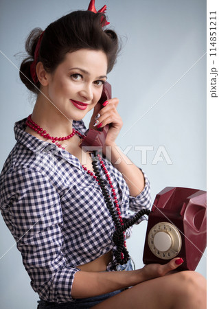 Woman in the style of the fifties. Beautiful retro girl talking on an old telephone. 114851211