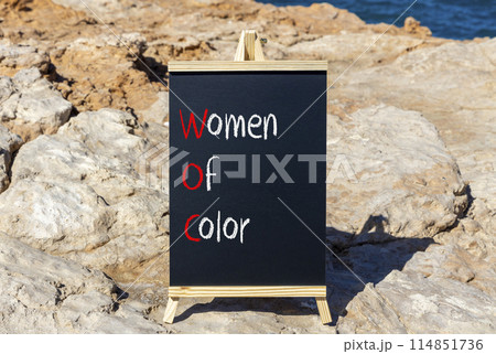 WOC women of color symbol. Concept words WOC women of color on beautiful yellow blackboard. Beautiful stone blue sky sea background. Business WOC women of color social issues concept. Copy space. 114851736