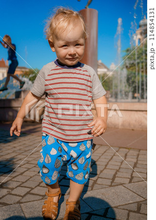 Child run and play on street fountain on Szombathely in Hungary. Boy have fun near fountain at Szombathely main square. Traveling in Szombathely city, Hungary. 114854131