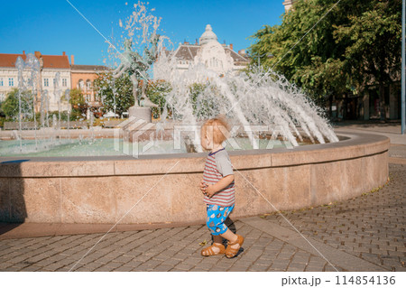 Child run and play on street fountain on Szombathely in Hungary. Boy have fun near fountain at Szombathely main square. Traveling in Szombathely city, Hungary. 114854136