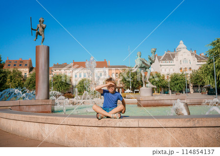 Child run and play on street fountain on Szombathely in Hungary. Boy have fun near fountain at Szombathely main square. Traveling in Szombathely city, Hungary. 114854137