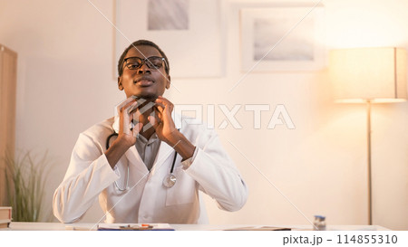 Telemedicine consulting. Doctor checkup. Professional male otorhinolaryngologist with stethoscope touching throat explaining diagnosis in modern interior with copy space. Telemedicine consulting. Doctor checkup. Professional male otorhinolaryngologist with stethoscope touching throat explaining diagnosis in modern interior with copy space. 114855310