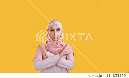 No gesture. Stop rejection. Refusing reaction. Concerned woman in hijab showing refusal crossed hands isolated on orange empty space background. No gesture. Stop rejection. Refusing reaction. Concerned woman in hijab showing refusal crossed hands isolated on orange empty space background. 114855326