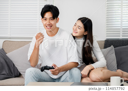 A man and woman are sitting on a couch playing a video game. The man is holding a controller and the woman is smiling. Scene is happy and relaxed A man and woman are sitting on a couch playing a video game. The man is holding a controller and the woman is smiling. Scene is happy and relaxed 114857792