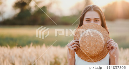 A woman is holding a straw hat and is hiding her face behind it. The image has a light and playful mood, as the woman is posing with the hat and making a silly face A woman is holding a straw hat and is hiding her face behind it. The image has a light and playful mood, as the woman is posing with the hat and making a silly face 114857806