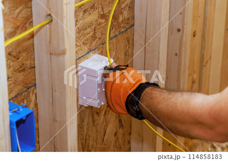 Electrical wiring of newly constructed building is connected to socket box by an electrician Electrical wiring of newly constructed building is connected to socket box by an electrician 114858183
