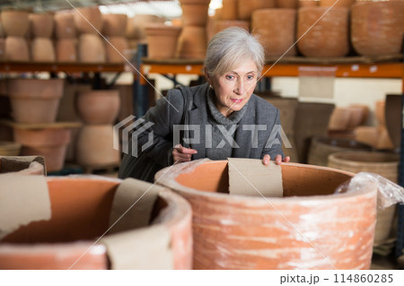 Aged woman selecting decorative earthenware pot in shop Aged woman selecting decorative earthenware pot in shop 114860285