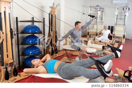 Girl is engaged in Pilates simulator with cable and ropes for stretching leg muscles Girl is engaged in Pilates simulator with cable and ropes for stretching leg muscles 114860334
