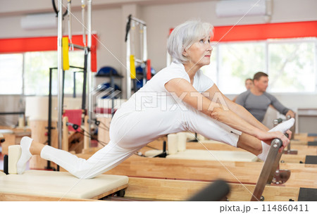 Senior woman performs exercise on reformer to improve coordination, balance, and posture 114860411