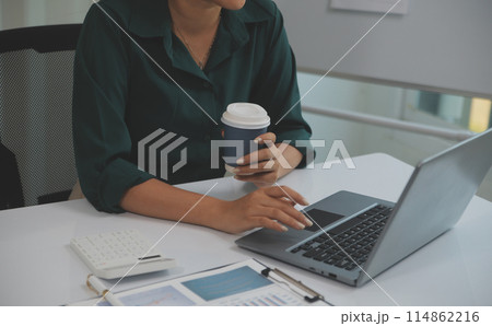 Beautiful young smiling Asian businesswoman working on laptop and drinking coffee, Asia businesswoman working document finance and calculator in her office. Beautiful young smiling Asian businesswoman working on laptop and drinking coffee, Asia businesswoman working document finance and calculator in her office. 114862216