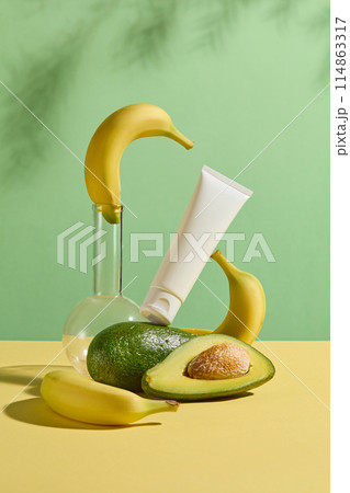 Photo has creative layout of avocado and banana theme with frontal shot, a boiling flask with a banana on top, an unlabeled cosmetic tube placed on a avocado and leaning on a banana, space for design Photo has creative layout of avocado and banana theme with frontal shot, a boiling flask with a banana on top, an unlabeled cosmetic tube placed on a avocado and leaning on a banana, space for design 114863317