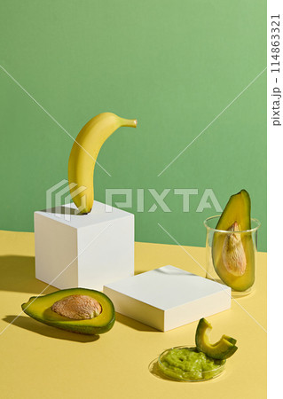 High angle shot photography against green background with yellow countertop contains rectangular white pedestals, yellow ripe banana and fresh avocado decorated around. Displaying and copy space 114863321