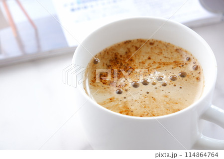 白いテーブルで、エスプレッソと牛乳を混ぜたカフェ・ラッテを飲みながら、雑誌を読んでいるイメージ 114864764