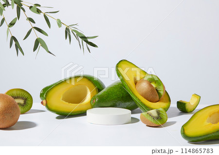 Against white background, a small podium in white color arranged with fresh kiwi fruits and avocado. Studio podium or platform product template mockup 114865783
